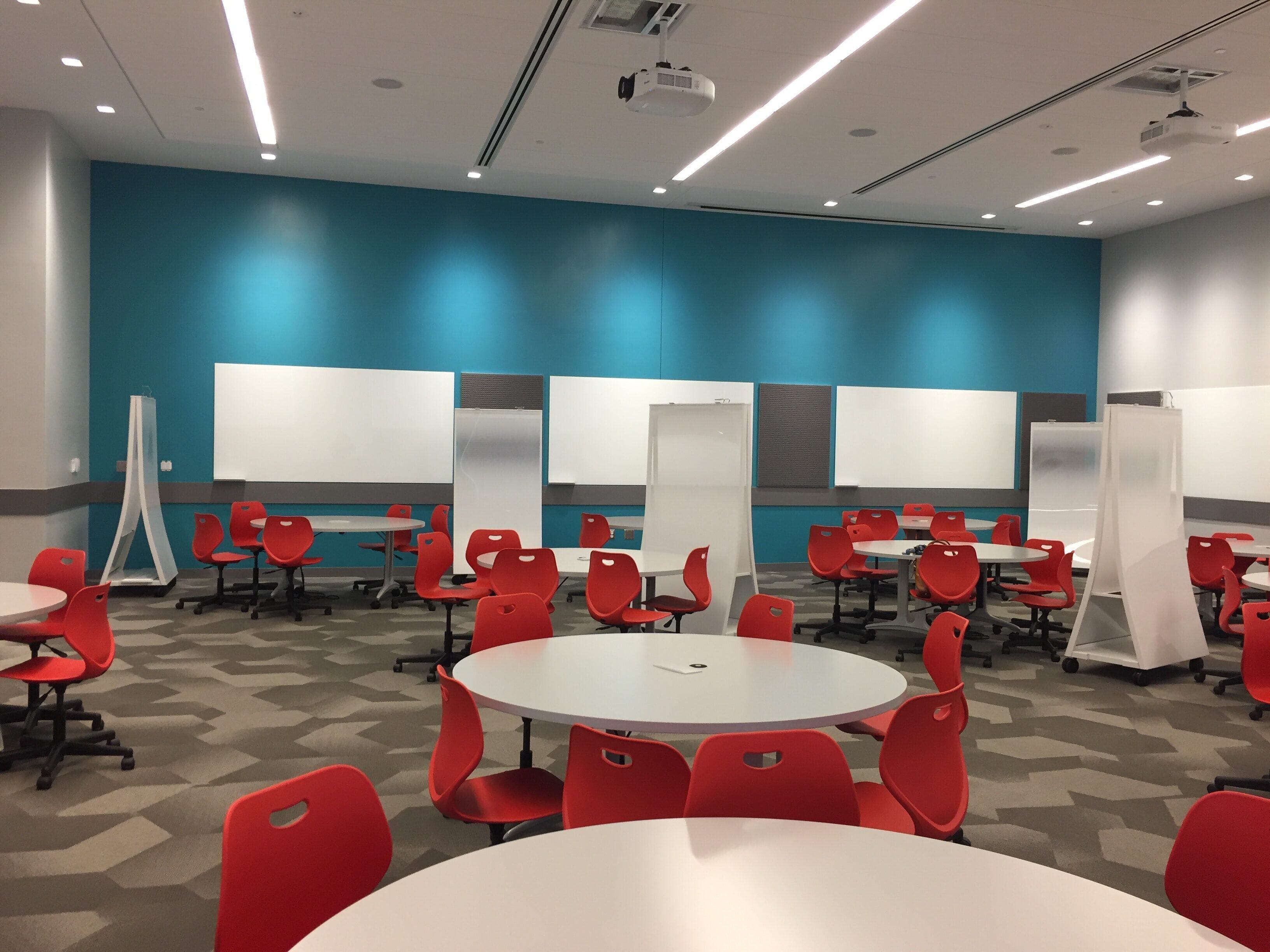 Room showing round tables with 6 chairs around each and moveable white boards on wheels