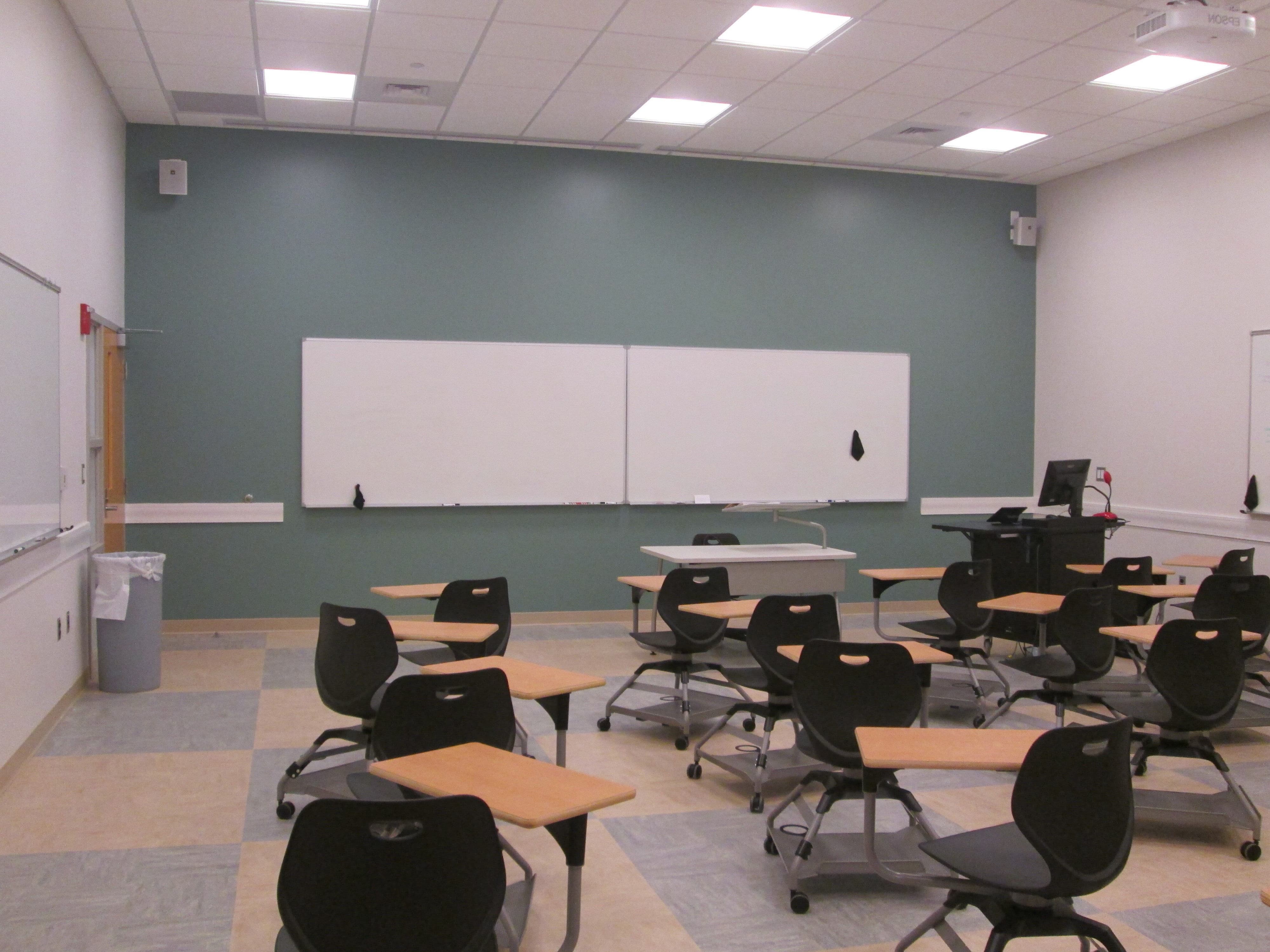 Room showing two fixed whiteboards on the wall and groupings of rolling tables with chairs designed to accommodate 2 students each