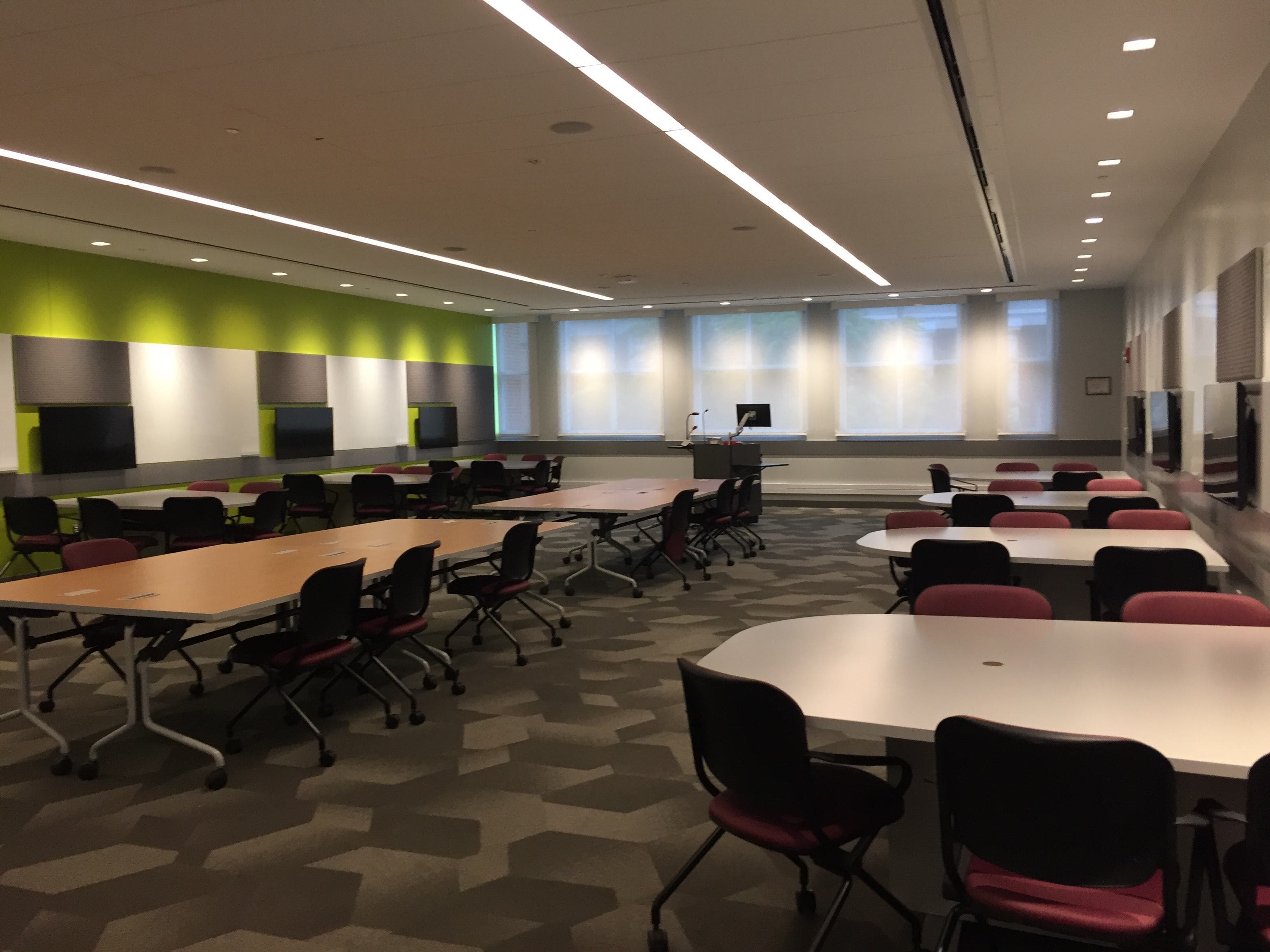 A large room with two long rectangular tables and several smaller tables arranged in rows with chairs on two sides of each table.